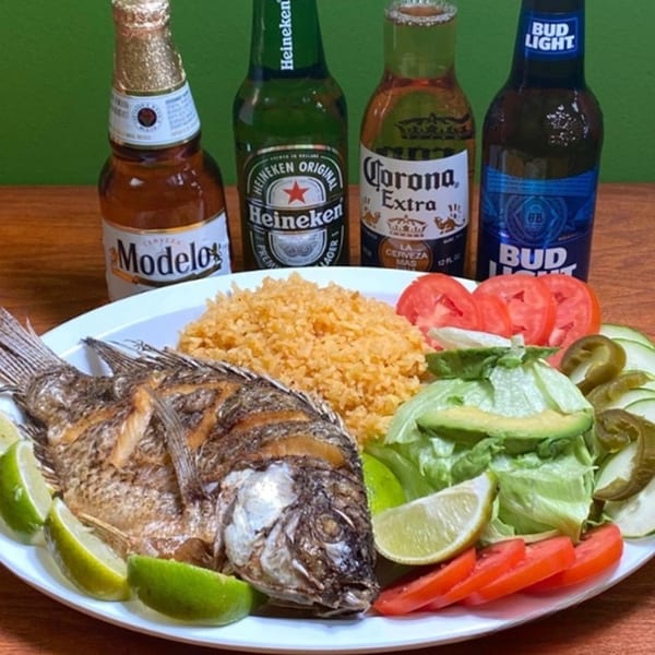 Fried fish with rice, salad, and lime wedges, accompanied by four bottles of beer.