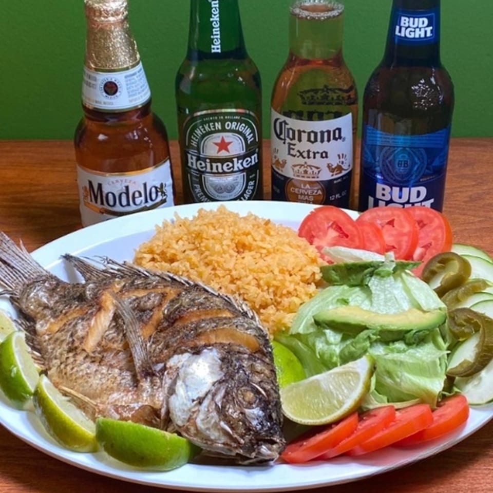 Fried fish with rice, salad, and lime wedges, accompanied by four bottles of beer.