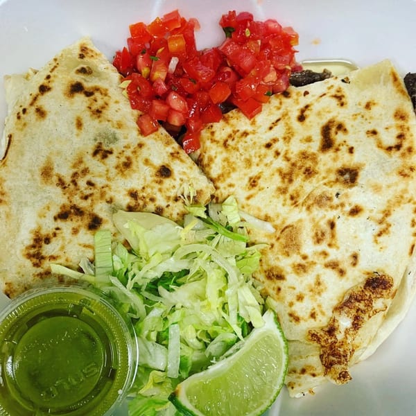 Two Tacos Al Carbon quesadillas with pico de gallo, shredded lettuce, lime, and green sauce.