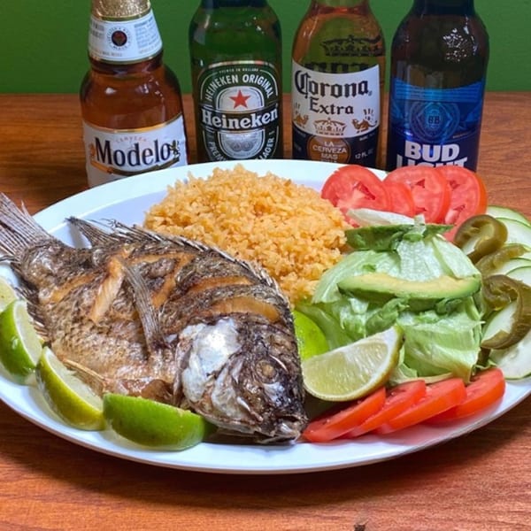 Fried fish with rice, salad, limes, and sliced tomatoes, with four beer bottles in the background.